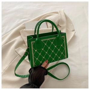 Detailed view of green square bag with heart embroidery and beige quilted patterns
