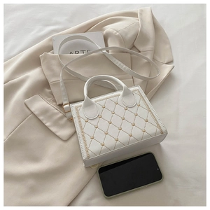 Detail of white quilted crossbody bag featuring heart embroidery and adjustable strap