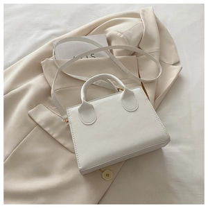 Detail of white square crossbody bag showing sleek leather texture and handle design