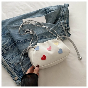 Detail of white canvas bucket bag with colorful heart patches and silver chain strap