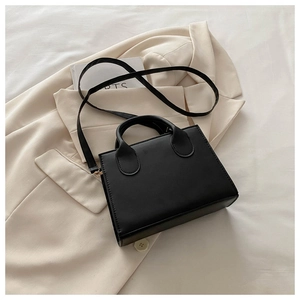 Detail of matte black leather square handbag on a beige blazer for stylish daily wear