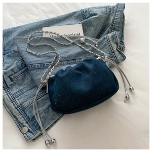 Close-up of pleated dark blue denim cloud bag with silver chain and metal bead detail