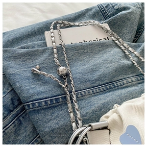 Detail of adjustable metal ball buckle on chain strap of a white pleated bucket bag