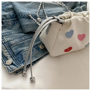 Close-up of white canvas mini cloud bag with colorful heart patches and silver chain strap