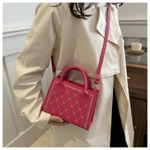Magenta underarm bag with heart quilting and adjustable strap worn on beige trench coat