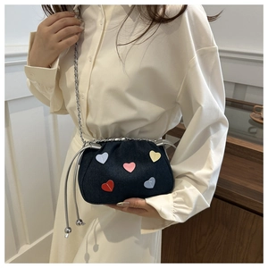 Detail of dark blue denim bucket bag with colorful heart patches and silver chain strap