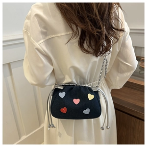 Detail of black canvas bucket bag with colorful heart patches and silver chain strap