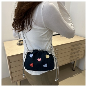 Detail of dark blue denim crossbody bucket bag with colorful heart patches and chain strap