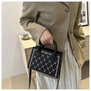 Close-up of black crossbody bag featuring white diamond stitching and small heart details