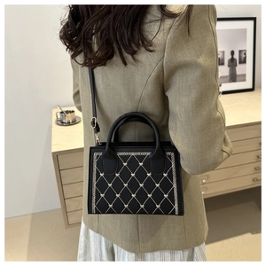 Detail of black quilted tote bag with heart embroidery worn with an olive blazer