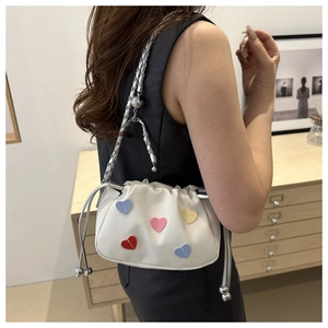 Detail of white canvas bucket bag with colorful heart patches and silver chain strap