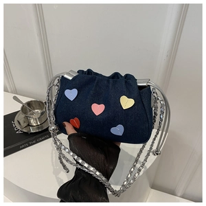 Detail of blue denim bucket bag featuring colorful heart patches and silver chain strap