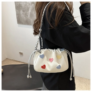 Detail of white canvas bucket bag featuring colorful heart patches and chain strap