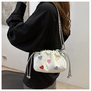 Detail of white canvas drawstring bucket bag with colorful heart patches and chain strap