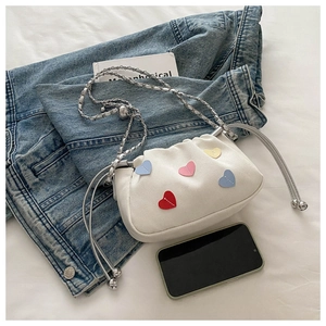 Detail of white pleated canvas shoulder bag with colorful heart patches and silver chain
