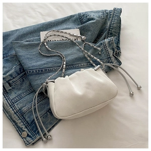 Detail of white pleated cloud bag with silver chain strap on denim and white sheet