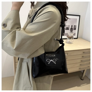 Détail du sac seau en cuir verni noir avec nœud argenté et bandoulière nouée