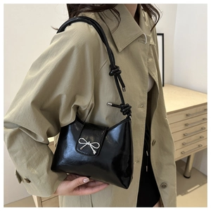 Détail d'un sac seau noir brillant avec un nœud en argent et une bandoulière nouée