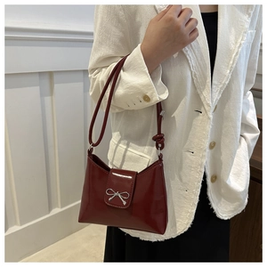 Détail du sac à main en cuir verni bordeaux avec nœud argenté sur blazer blanc
