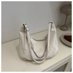 Detail of off-white cloud bag texture with silver chain and wide strap on a desk