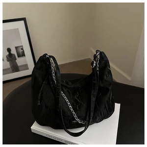 Detail of black pleated shoulder bag with silver chain on books, minimalist aesthetic