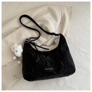 Detail of black pleated crescent shoulder bag with silver chain and white plush charm
