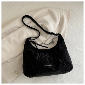 Detail of black pleated shoulder bag with silver chain on white blazer background