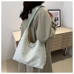 Detail of white textured tote bag with green strap worn by model in minimalist room