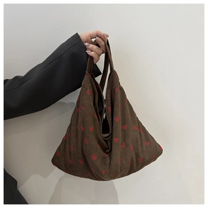 Detail of brown corduroy tote bag with strawberry pattern held by a model