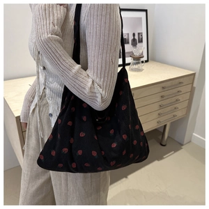 Black corduroy tote bag with red strawberry pattern shown on shoulder by a model