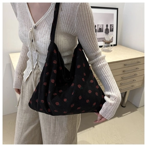 Detail of strawberry print on black corduroy tote bag showing textured fabric and strap