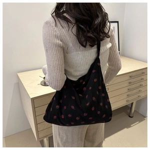 Close-up of black corduroy tote bag featuring red strawberry patterns on a wide shoulder strap
