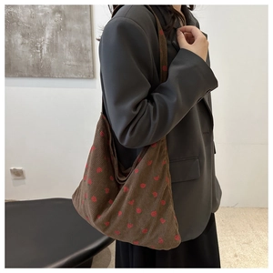 Detailed close-up of brown corduroy shoulder bag featuring strawberry embroidery on model