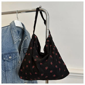 Detail of strawberry print on black corduroy shoulder bag hanging next to denim jacket