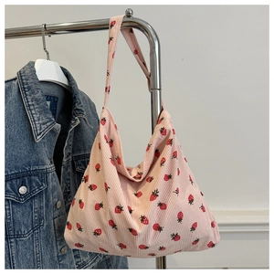 Detail of pink corduroy tote bag featuring strawberry prints hanging on a metal rack