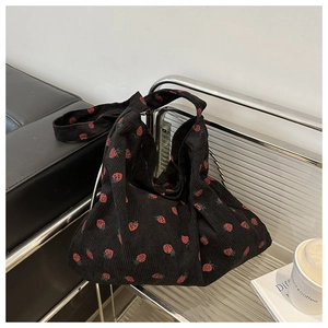 Detail of black corduroy hobo bag with red strawberry print on a transparent chair