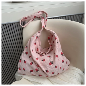 Detailed view of pink corduroy shoulder bag with strawberry prints on a white chair