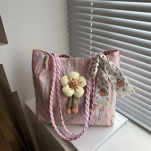 Pink jacquard tote bag with floral charm and patterned silk scarf on white surface