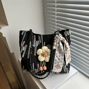 Black woven tote bag with colorful wave embroidery and a 3D floral charm detail