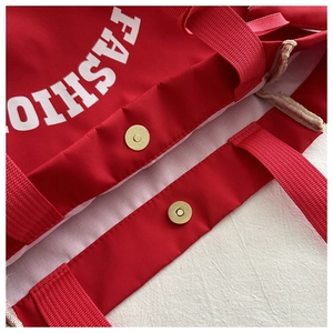 Vue détaillée du fermoir magnétique doré et de la couture du sac cabas en toile rouge