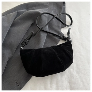 Close-up of black suede crescent bag showing pleated texture and knotted shoulder strap
