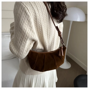 Close-up of a brown pleated crescent bag featuring stylish knotted strap and tassel detail