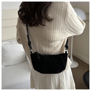 Detail of black suede dumpling bag with knot shoulder strap worn by a model