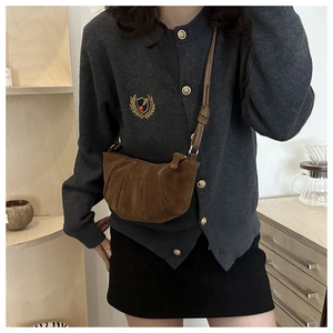 Brown suede crescent bag with pleated design worn as a crossbody in a cozy setting