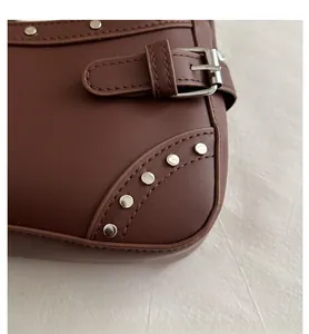 Close-up of dark brown leather shoulder bag featuring silver rivets and adjustable buckle strap