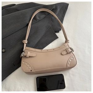 Detail of beige baguette underarm bag with silver rivets and leather buckle beside phone