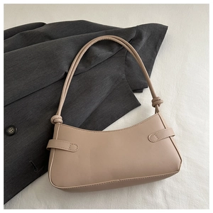 Chic beige leather underarm bag featuring decorative knots and curved opening on a blazer