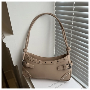 Close-up of beige crescent bag featuring punk rivets and metallic buckle details