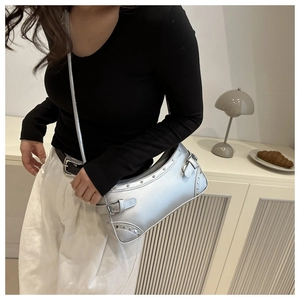 Silver Y2K baguette bag with metallic rivets and buckles worn by model in a minimalist setting