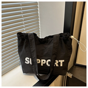 Détail d'un grand sac cabas noir avec impression de lettres SUPPORT blanches en gras